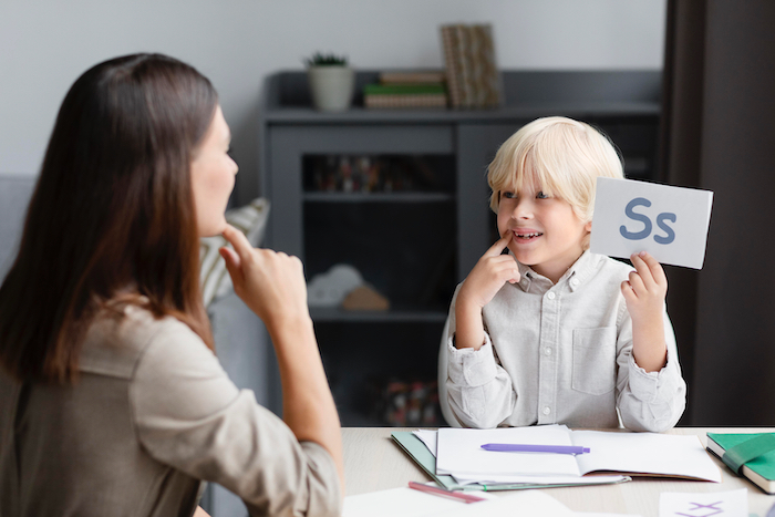 A Speech Therapist and a boy are sitting and doing articulation exercises for the letter S