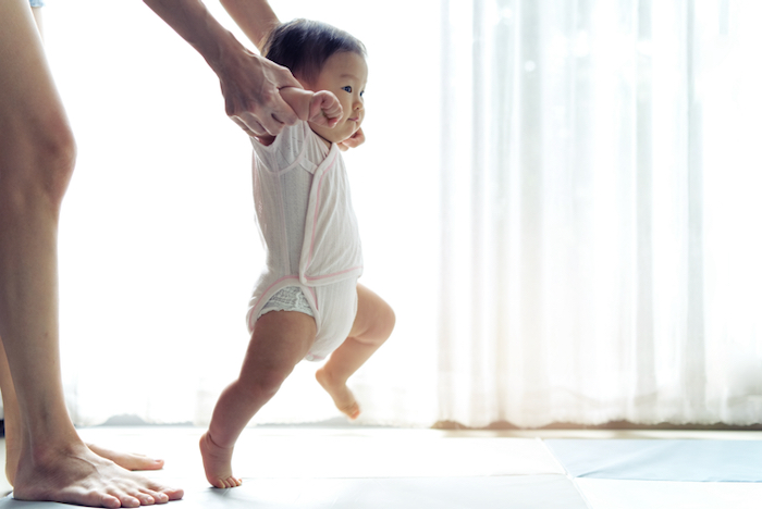 A baby takes his first steps with the support of the parent