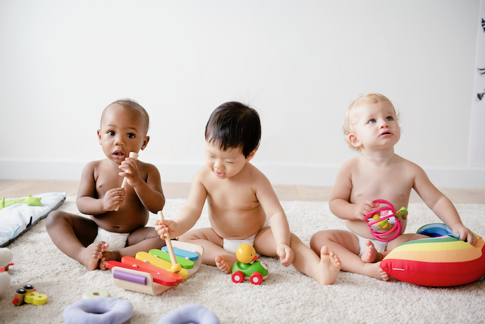 Three babies are on the floor playin different toys