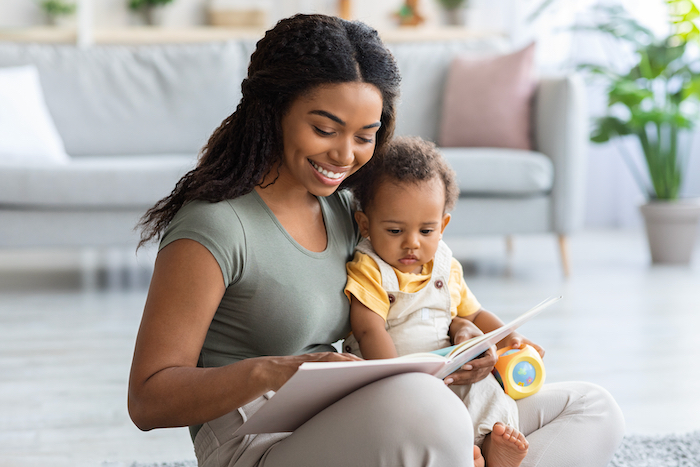 Mum is reading a book to her baby, while it is sitting on her lap