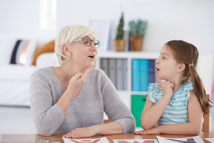 Girl is next to her therapist on a speech therapist session working on stuttering