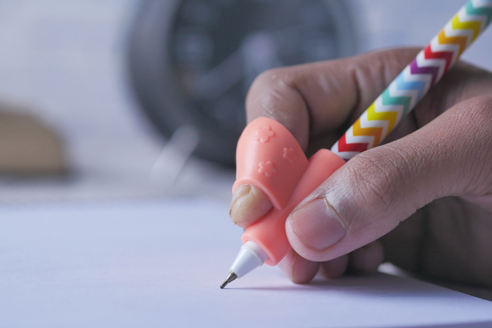 kid is writing using a pencil grip aid