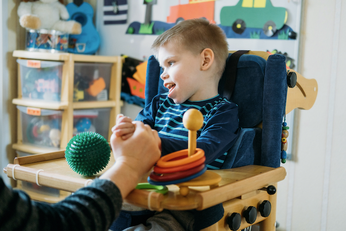 Boy with cerebral palsy sitting in a special chair and doing therapeutic activities.